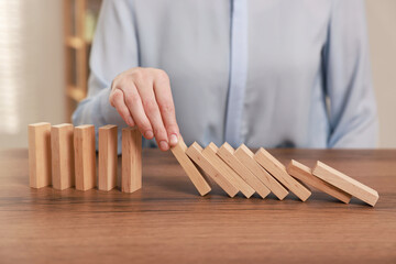 Woman stopping wooden blocks from falling at table, closeup. Domino effect