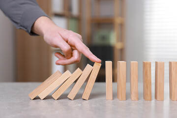 Woman stopping wooden blocks from falling at table, closeup. Domino effect