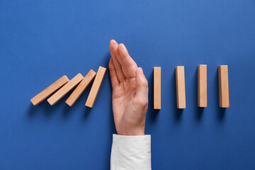 Man stopping wooden blocks from falling on blue background, top view. Domino effect