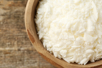 White soy wax flakes in bowl on wooden table, closeup