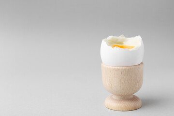 Soft boiled egg in cup on light grey background, space for text