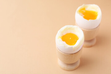Soft boiled eggs in cups on beige background, closeup. Space for text