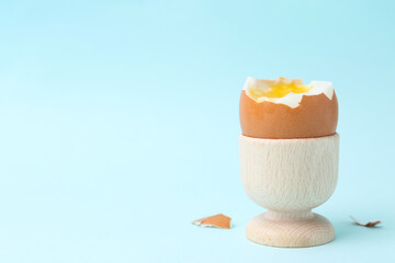 Soft boiled egg in eggcup on light blue background, closeup. Space for text
