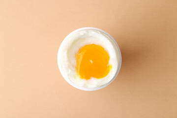 Soft boiled egg in cup on beige background, top view