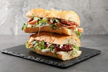 Halves of baguette sandwich with prosciutto and sun dried tomatoes on grey table