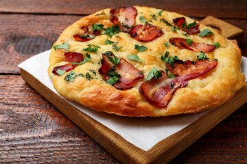 Delicious focaccia bread with bacon and parsley on wooden table, closeup