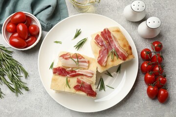 Pieces of delicious focaccia bread with bacon served on grey table, flat lay