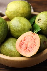 Fresh cut and whole guava fruits in bowl on table, closeup