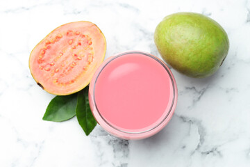 Tasty guava juice in glass, leaves and fruits on white marble table, flat lay