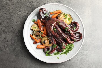 Roasted octopus with vegetables and mushrooms on grey table, top view