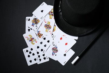 Playing cards, hat and magic wand on black background, top view
