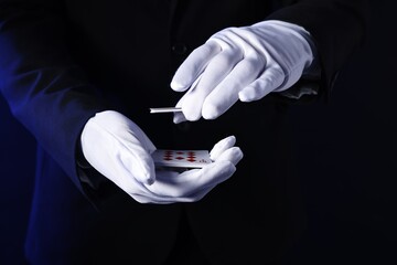 Illusionist shuffling playing cards on dark blue background, closeup