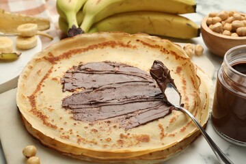 Tasty crepes with chocolate butter, bananas and hazelnuts on table, closeup