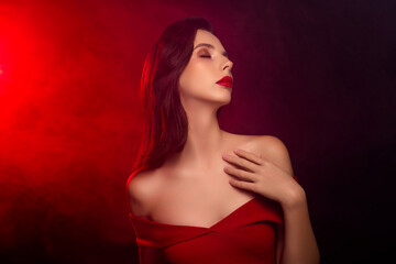 Fototapeta premium Elegant woman in red dress with sensual expression against dramatic red and black background