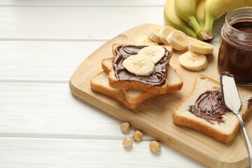 Sandwiches with chocolate butter, bananas and hazelnuts on white wooden table, closeup. Space for text