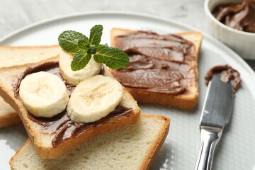 Sandwiches with chocolate butter, banana, mint and knife on table, closeup