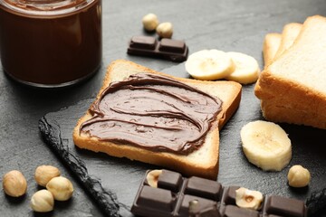 Sandwich with chocolate butter, banana and hazelnuts on black table, closeup