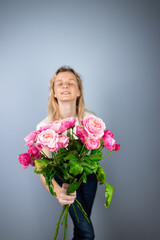 on a light gray background a young blonde girl with a large bouquet of pink peony roses women's holiday March 8 first date emotions on the face smiling girl leaning forward to the camera