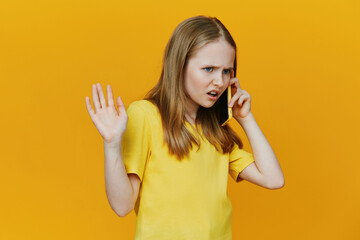 Angry girl talking on the phone with a yellow background, expressing frustration, casual wear,...