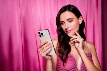 Stunning woman in pink dress using smartphone against glamorous pink draped background