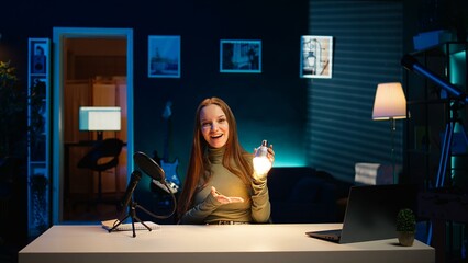 Content creator presenting light bulb in home studio, filming with professional equipment. Young teenager doing influencer marketing in apartment, presenting lighting gear, camera B