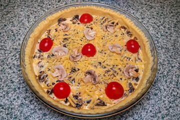 Quiche tart in the process of cooking before baking. Sliced ​​mushrooms, yellow grated cheese and red cherry tomatoes on shortcrust pastry