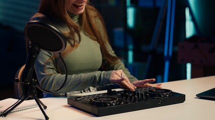 Young artist films DJ mixing tutorial in apartment studio, showing examples of sampling on sound controller. Happy entertainer shows modern musical equipment to subscribers in living room, camera A