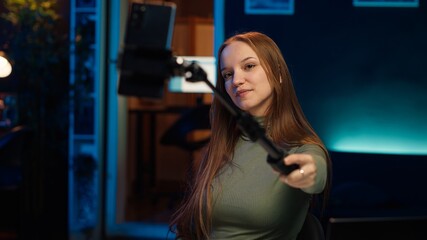 Young content creator using cellphone to film room tour to subscribers watching her. Teenage entertainer doing video presenting apartment to fans, recording with phone on selfie stick, camera A