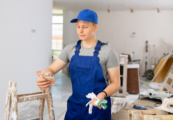 Satisfied young man in blue overall holding bunch of cash he obtained for first part-time job in building site. Boy got his first wage.