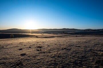 Sunrise over a frost covered field highlighting the tranquil beauty of a serene landscape The sun rises behind distant hills