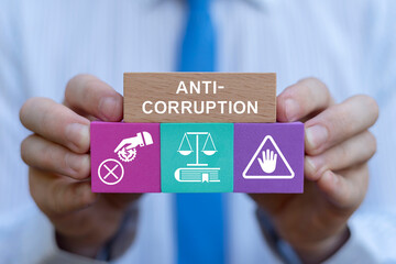Business person holding colorful blocks with icons sees inscription: ANTI-CORRUPTION. Concept of anti corruption activities that oppose or inhibit corruption. International anti-corruption day.