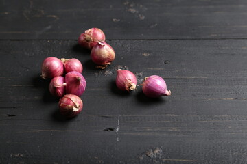 Several fresh purple shallots, some peeled and some unpeeled, arranged on a dark wooden surface for food and ingredient photography.
