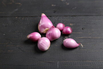 Several fresh purple shallots, some peeled and some unpeeled, arranged on a dark wooden surface for food and ingredient photography.