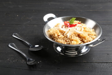 Authentic Indonesian fried rice with shredded chicken and chili, served in a metal bowl on dark wood with cutlery. Ideal for food themes, menus, or culinary promotions.