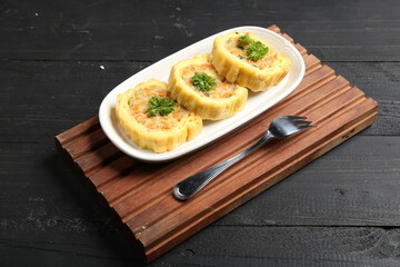 Top view of vegetable-stuffed egg rolls served on a white plate with parsley garnish and a fork on wooden tray, delicious Asian-style savory snack on rustic dark background.