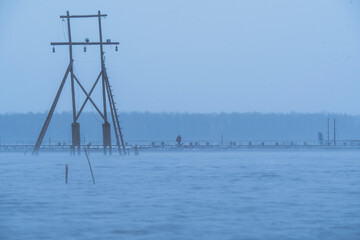 Foggy lake with wooden structure and distant pier in cold blue tones