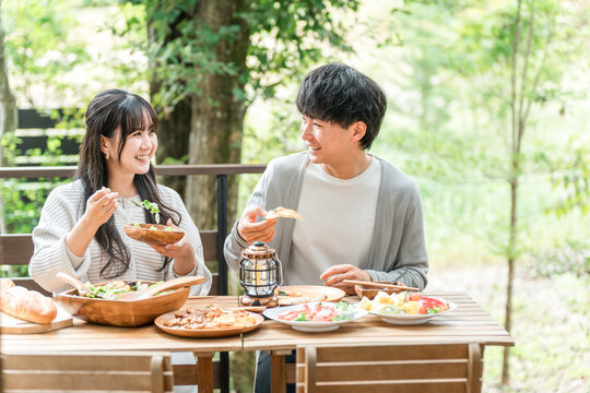 ウッドデッキ・テラス席・バルコニー席で食事するカップル・夫婦（グランピング・ベランピング）
