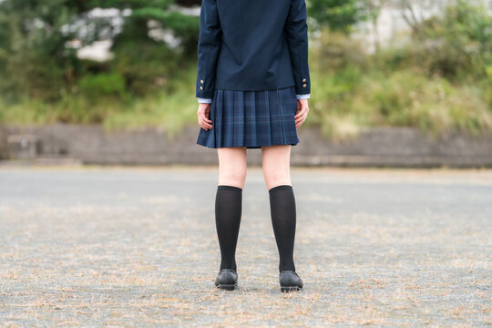 学校の校舎の前に立つ制服姿の中学生・高校生・小学生の後ろ姿
