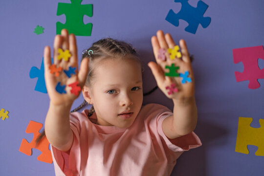 A lonely girl on a purple studio background shows pieces of colorful puzzles with her arms outstretched. World Autism Awareness Day - Powered by Adobe