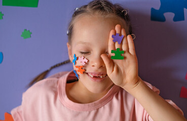A laughing cute girl with eyes closed hides part of face behind hand with puzzles. Overcoming the deficit of emotional expressions and communication in children with autism - a concept