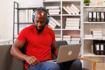 African American man is wearing headphones using laptop and working in the living room

