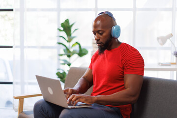 African American man is wearing headphones using laptop and working in the living room
