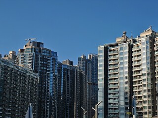 Obraz premium Dense cluster of Hong Kong apartment buildings and houses under a clear blue sky. Modern high-rise structures rise towards the sky.