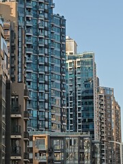 Fototapeta premium Dense Hong Kong apartment buildings rise into a clear blue sky. Numerous balconies and windows are visible on these high-rise residential structures.