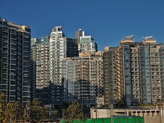 Fototapeta premium Dense Hong Kong apartment buildings rise against a clear blue sky. Numerous high-rise residential structures create a cityscape of houses packed closely together.