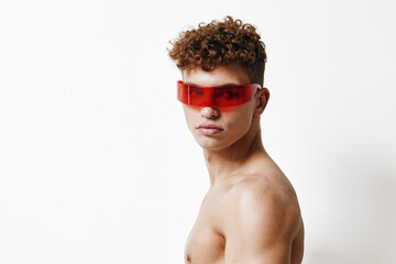 Stylish young man with curly hair wearing red sunglasses, striking a confident pose against a white...