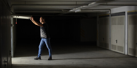 40 year old white European male with athletic build opening garage door with light from inside hitting his body