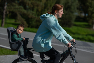 Caucasian woman riding a bicycle with her toddler son sitting behind her in a child seat. 