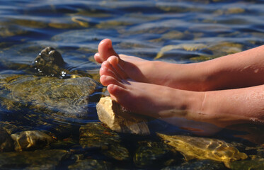 Teenager girl relaxing in water, barefoot in clear cool water. Healthy lifestyle. Young woman enjoying nature on the beach. Ripple patterns reflect light on water over pebbles,