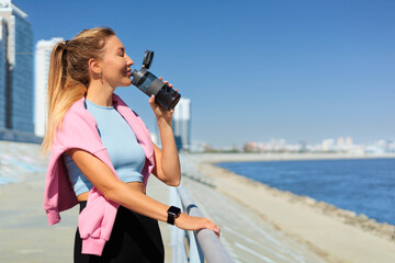 Sport woman jogger runner drinking water from bottle at city embankment river closeup